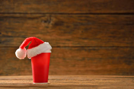 Paper coffee cup with santa's hat on top on wooden backgroundの写真素材