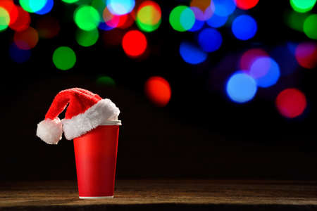 Paper coffee cup with santa's hat on top on bokeh background of Christmas lightsの写真素材