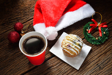 Paper coffee cup and cake surrounded by Christmas decorations on wooden backgroundの写真素材