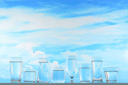 Fresh and clean drinking water in assortment of glasses on sky backgroundの写真素材