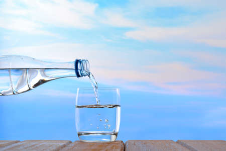 Fresh and clean drinking water being poured from bottle into glass on sky backgroundの写真素材