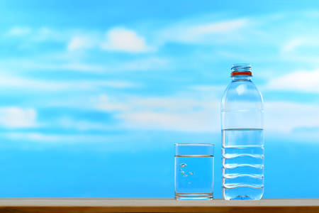 Fresh and clean drinking water in bottle and glass on sky backgroundの写真素材