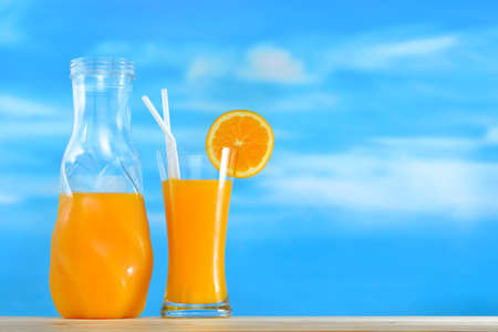 Orange juice in jug and glass on sky backgroundの写真素材