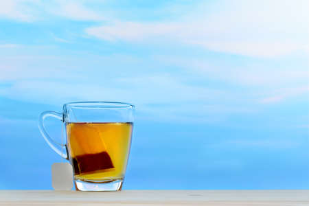 Cup of tea with tea bag on sky background