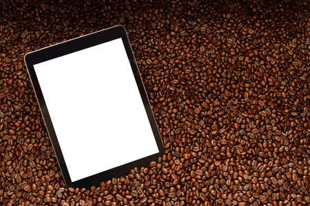 Tablet computer with blank white screen on pile of coffee beansの写真素材