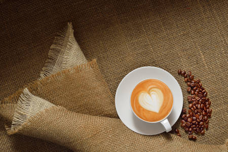 Top view of cup of coffee latte and coffee beans on burlap background