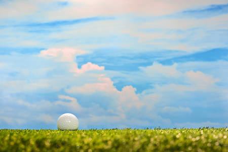 Golf ball on green grass on sky backgroundの写真素材