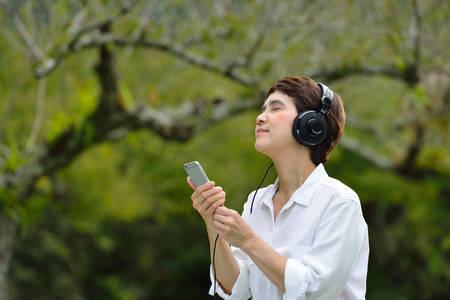 Middle age woman enjoying music from smartphone with headphones in the park