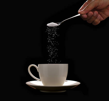 Hand putting sugar in coffee cup on black backgroundの写真素材