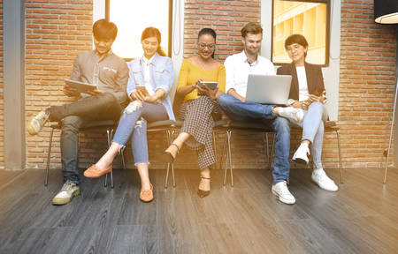 Group of businesspersons with age variety holding electronic devices and gadgets in the officeの写真素材