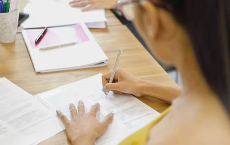 Businesswoman writing on document sitting in the officeの写真素材