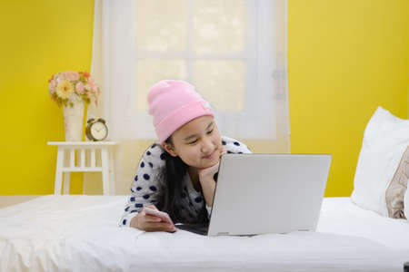 Young beautiful smiling  teenage girl using laptop computer and smartphone lying on bedの写真素材