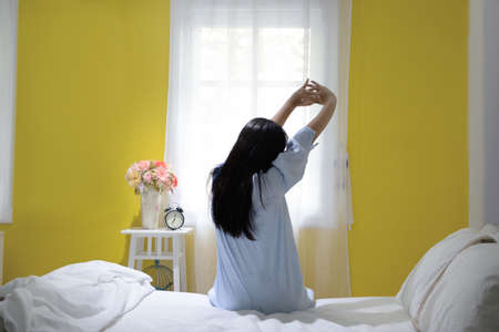 Woman stretching in bed after wake up, back viewの写真素材