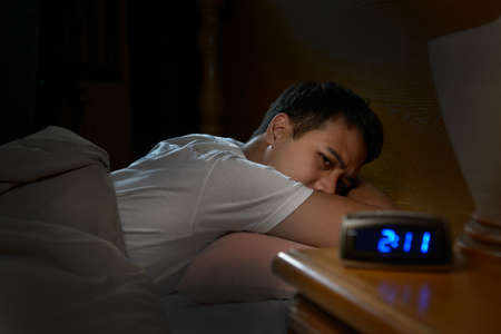 Depressed man suffering from insomnia lying in bedの写真素材