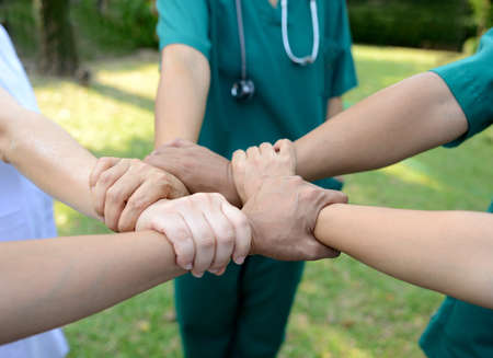 Doctors and nurses in a medical team stacking hands outdoor on the green park background (volunteer)の写真素材