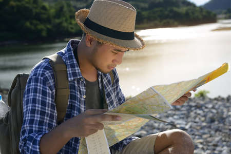 Young Asian tourist man with backpack looking at the map with natureの写真素材