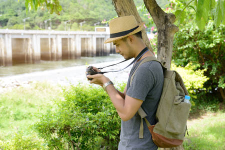 Young Asian tourist man with backpack looking at a camera with resevoir and naturalの写真素材