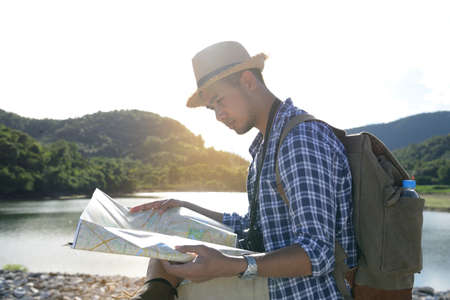 Young Asian tourist man with backpack looking at the map with nature background