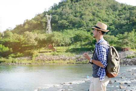 Young Asian tourist man with backpack traveling and enjoying on the river bankの写真素材