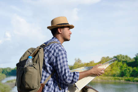 Young Asian tourist man with backpack and map looking at the natureの写真素材