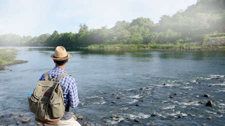 Young Asian tourist man with backpack traveling along river bankの写真素材
