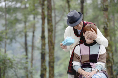 Happy senior man surprises wife with present outdoorの写真素材