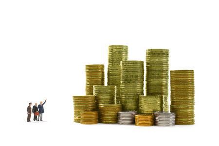 Miniature businessmen looking and pointing at stack of coins on white background for business,...