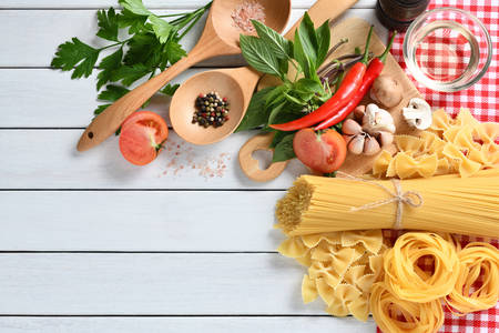 Pasta spaghetti, farfalle, linguine with vegetables and spices on white wooden tableの写真素材
