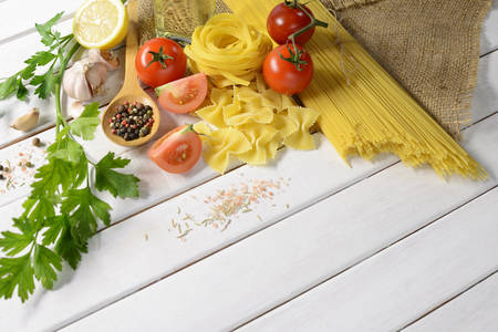 Pasta spaghetti, farfalle, linguine with vegetables and spices on white wooden tableの写真素材