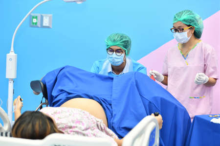 Asian male obstetrician and nurse are delivered to the patient lying on a bed in the delivery room of the hospitalの写真素材