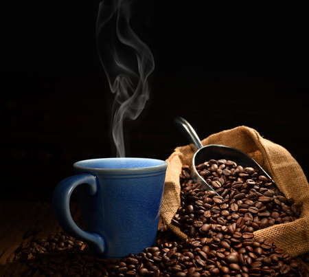 Cup of coffee with smoke and coffee beans on black background