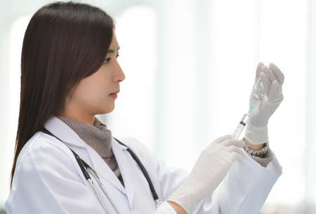 Smiling Asian medical doctor woman holding syringe with medicine in hospital with copy spaceの写真素材