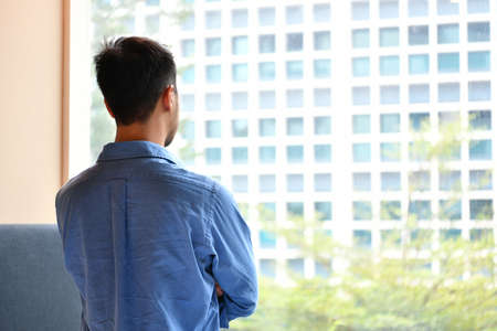 Young man looking out of the window in  the roomの写真素材