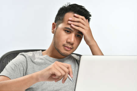 Casually-dressed startup business man holding his head looking stressed while working on a laptop