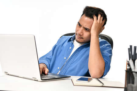 Casually-dressed startup business man holding his head looking stressed while working on a laptop