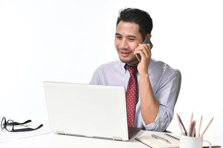 Young businessman smiling while talking on the phone and working with laptop computerの写真素材