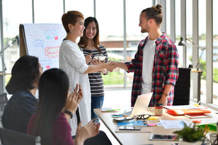 Two businesspersons shaking hands in agreement with congratulating colleaguesの写真素材