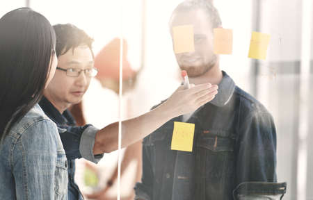 Business persons discussing work on a glass board with other colleagues in the background at the officeの写真素材
