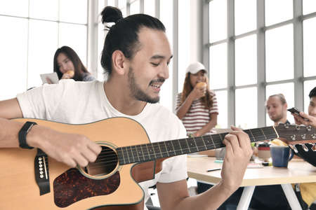 Group of business persons relaxing, playing guitar and chatting during break time at the office