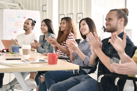 Group of businesspersons cheering and clapping for a co-worker at the office