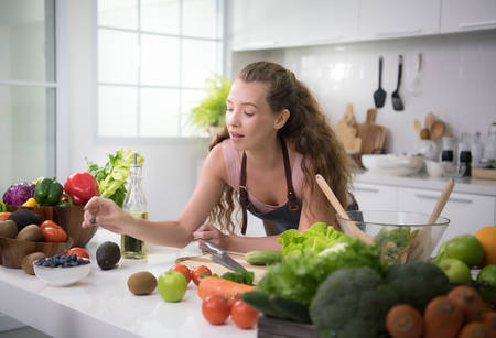 Healthy young woman in a kitchen preparing vegetables for healthy meal and saladの写真素材