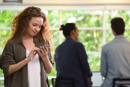 Young businesswoman using smartphone in the office with colleagues in the background