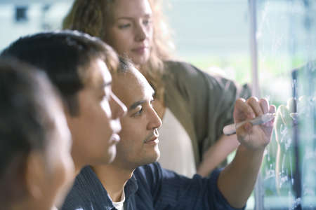 Group of businesspersons discussing work and using glass board in the office