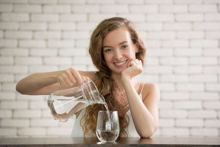 Young woman pouring water from jug into glass in the room
