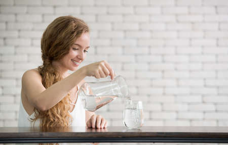 Young woman pouring water from jug into glass in the room