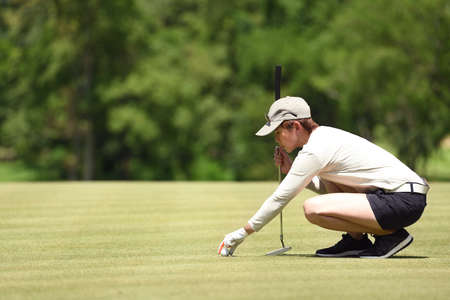Woman golfer check line for putting golf ball on green grassの写真素材