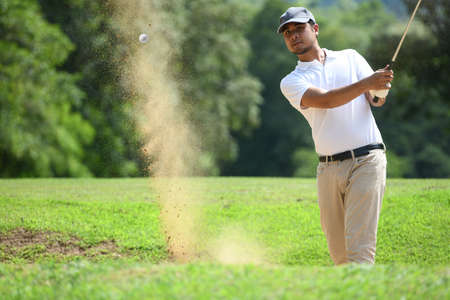 Young Asian man golfer hitting a bunker shotの写真素材