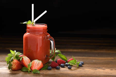 Mixed berry smoothie in glass with sliced berries on wooden background