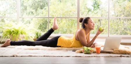 Healthy Asian woman lying on the floor eating salad looking relaxed and comfortable