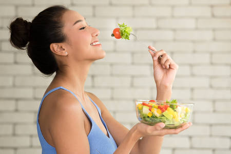 Asian woman in joyful postures with hand holding salad bowlの写真素材